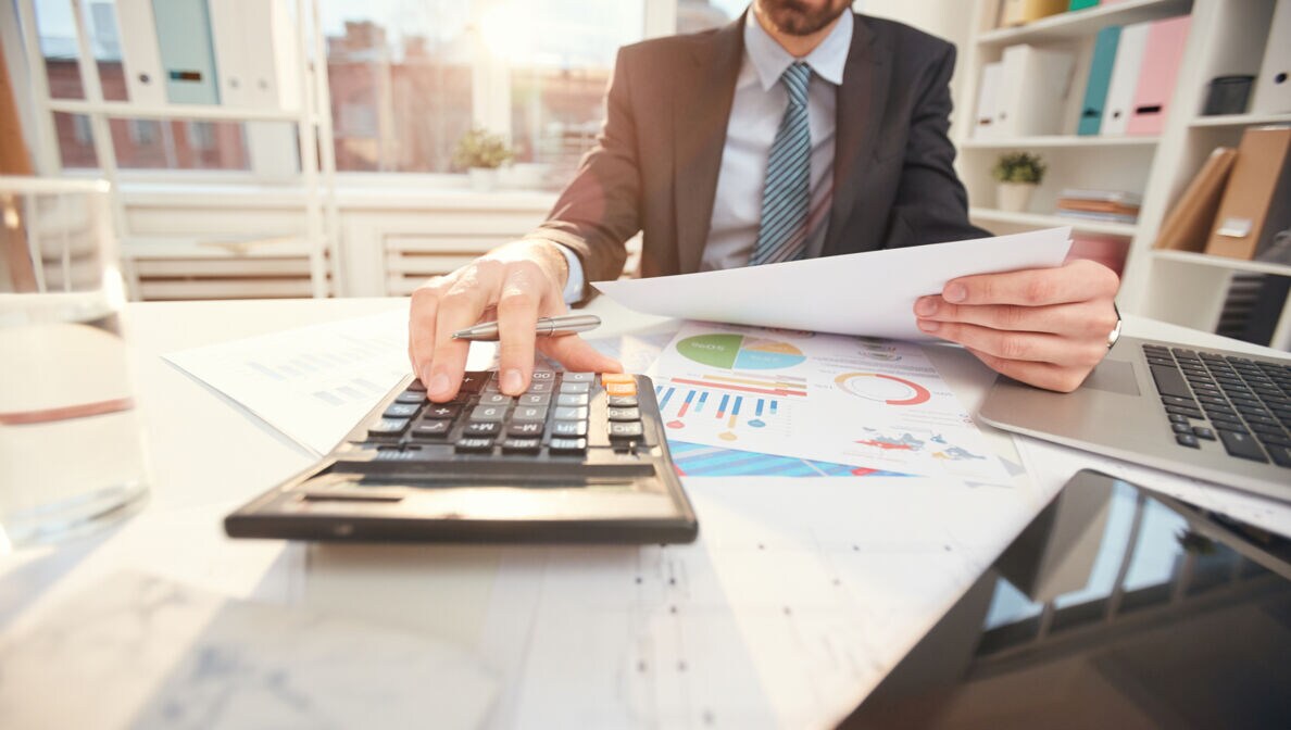 Ein Mann sitzt in einem Büro und gibt etwas in einen Taschenrechner ein