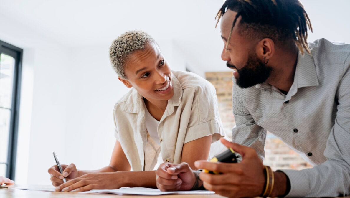 Eine Frau, die einen Vertrag unterzeichnet und dabei und einen Mann neben ihr anlächelt