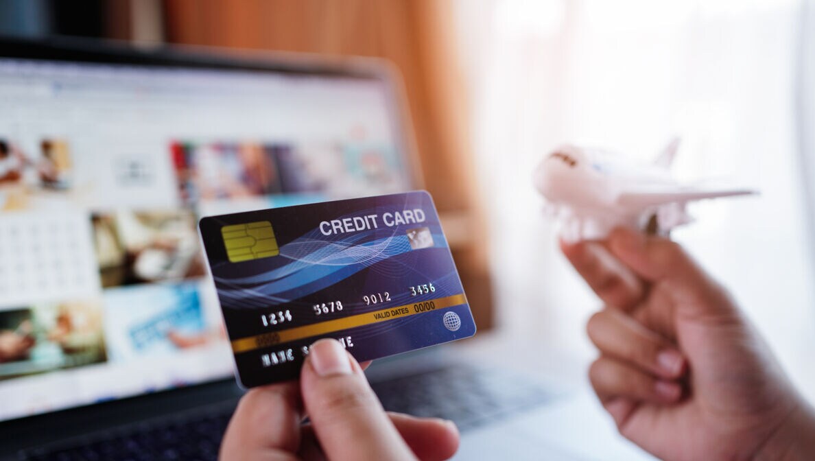 Zwei Hände, eine Kreditkarte und ein Flugzeugmodell haltend, vor einem Laptopbildschirm