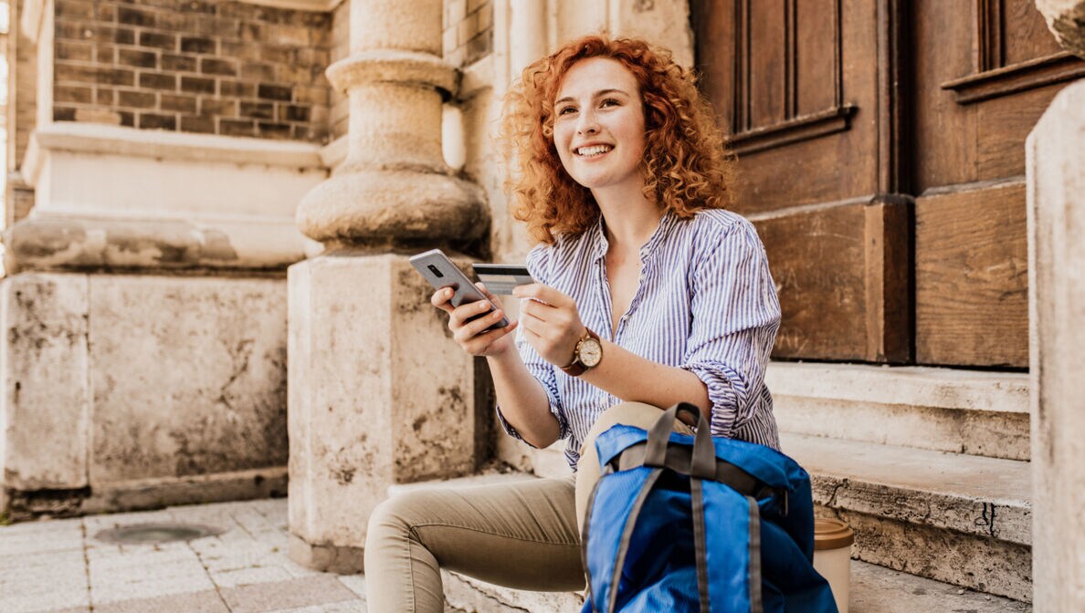 Junge Frau auf einer Treppe sitzend mit Kreditkarte und Smartphone in der Hand