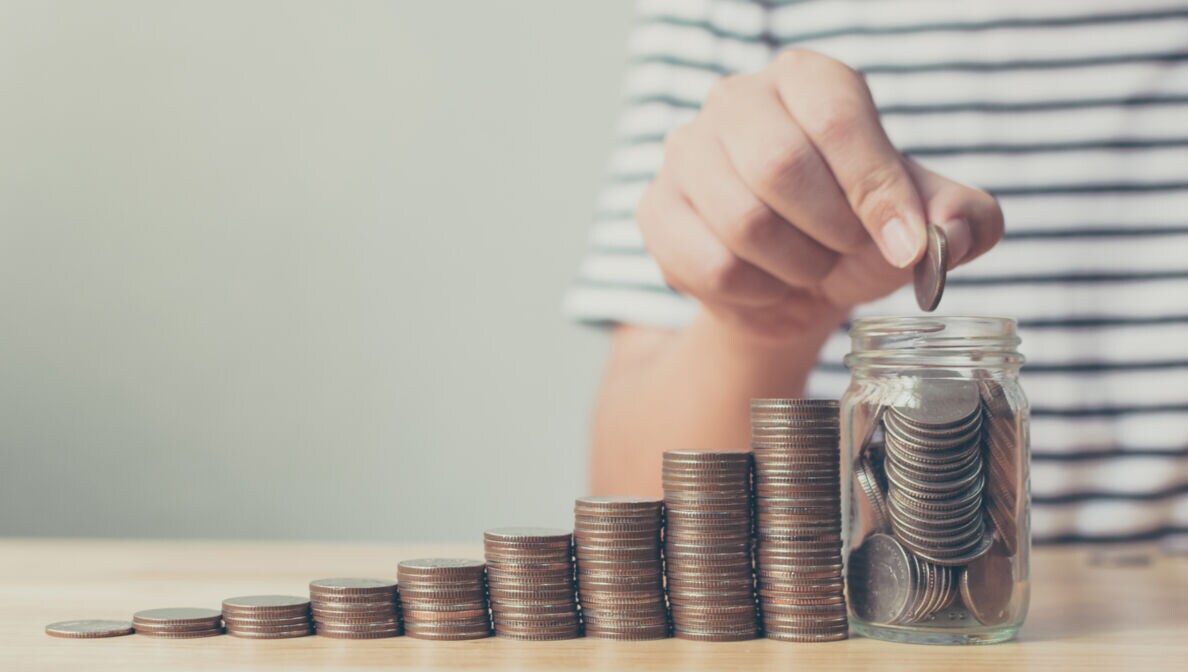 Von links nach rechts höher werdende Münzstapel und ein mit Geld gefülltes Glas
