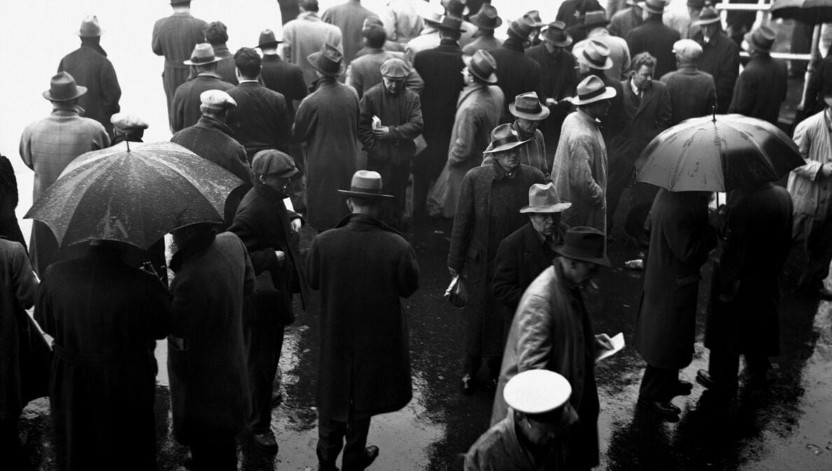 Schwarz-Weiß-Bild von Männern in Mänteln und Hüten, die im Regen auf der Straße stehen