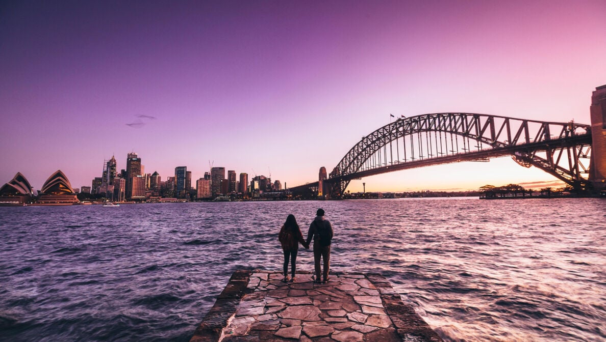 Eine Frau und ein Mann stehen gegenüber der australischen Stadt Sydney und schauen auf die Skyline.