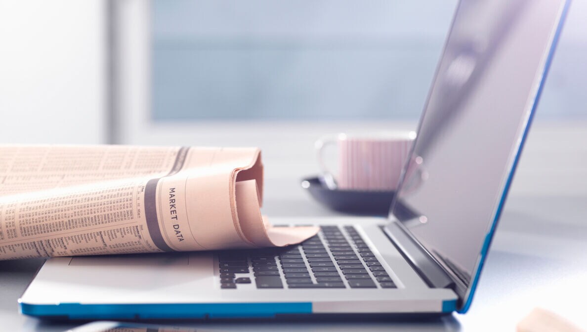 Auf einem Laptop liegt eine Zeitung mit Börsendaten