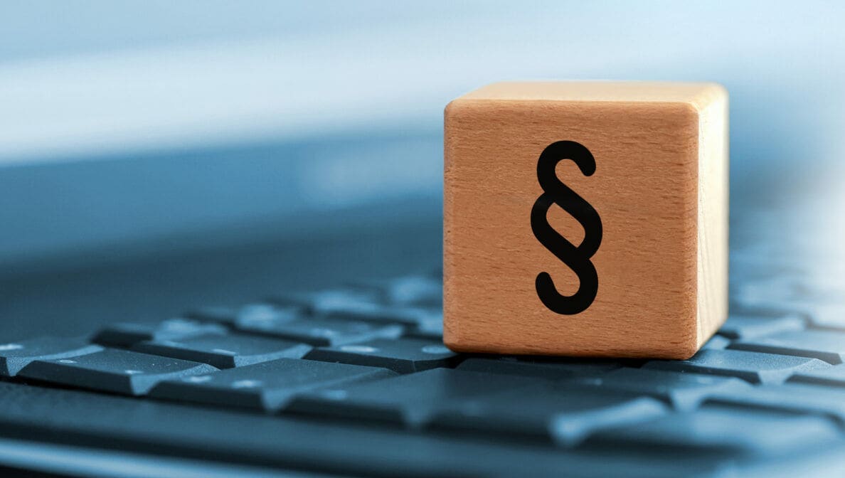 Ein Holzwürfel mit einem Paragrafenzeichen steht auf einer Laptoptastatur.