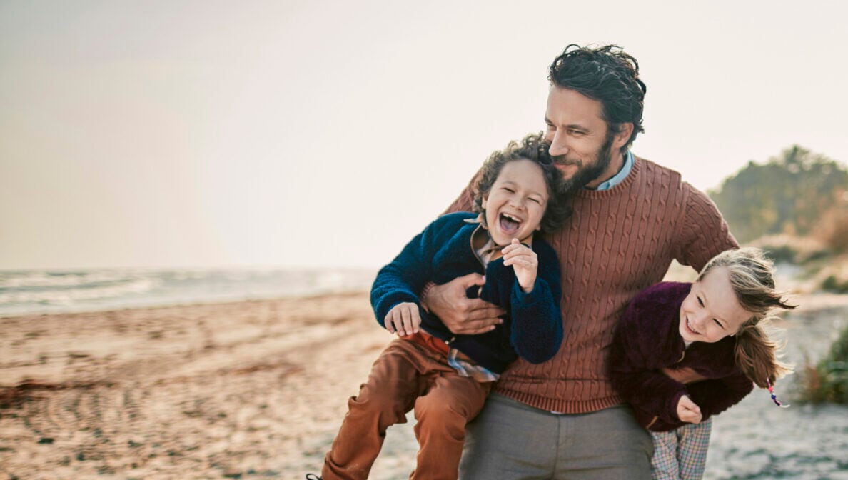 Ein Mann mit zwei lachenden Kindern im Arm am Strand