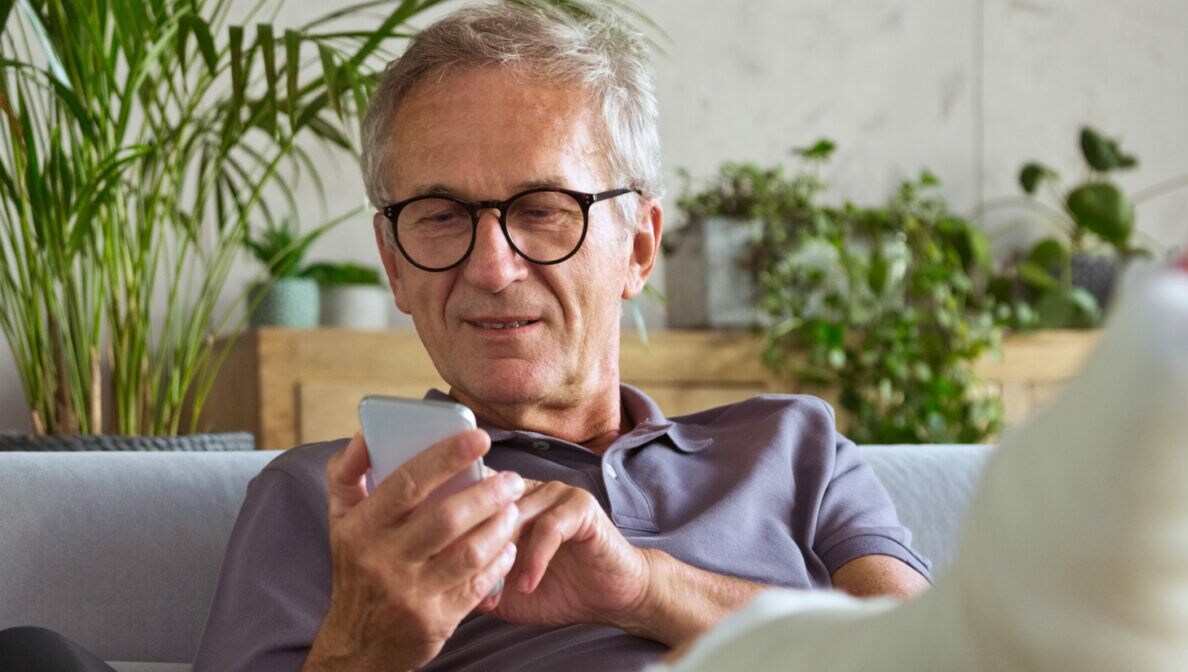 Ein Mann auf einem Sofa, der ein Smartphone in der Hand hält und seinen eingegipsten Fuß hochlegt