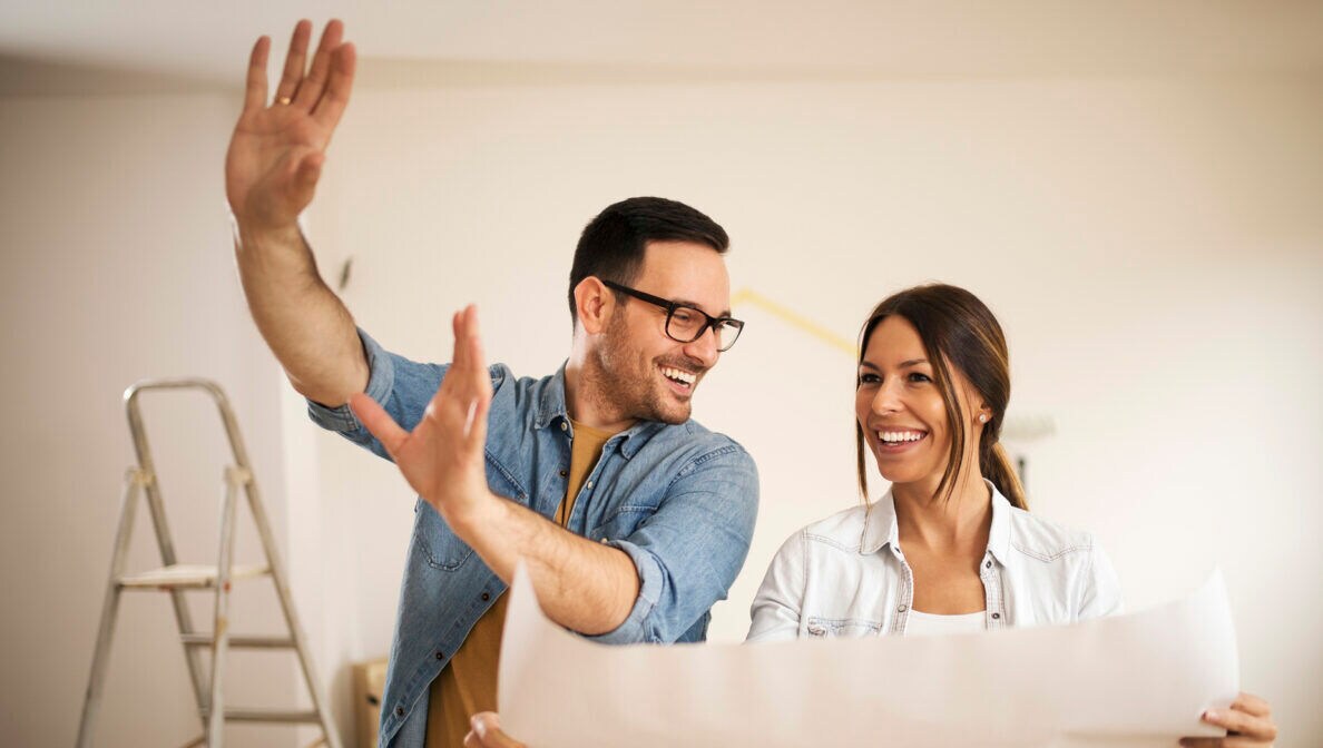 Ein Paar steht in einem leeren Zimmer und schaut auf Pläne zum Umbau seines Hauses.