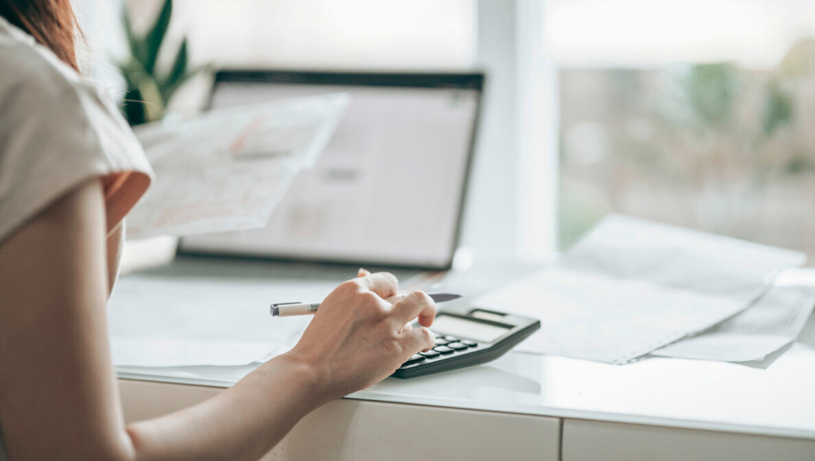 Eine Person am Schreibtisch, die etwas in einen Taschenrechner eintippt