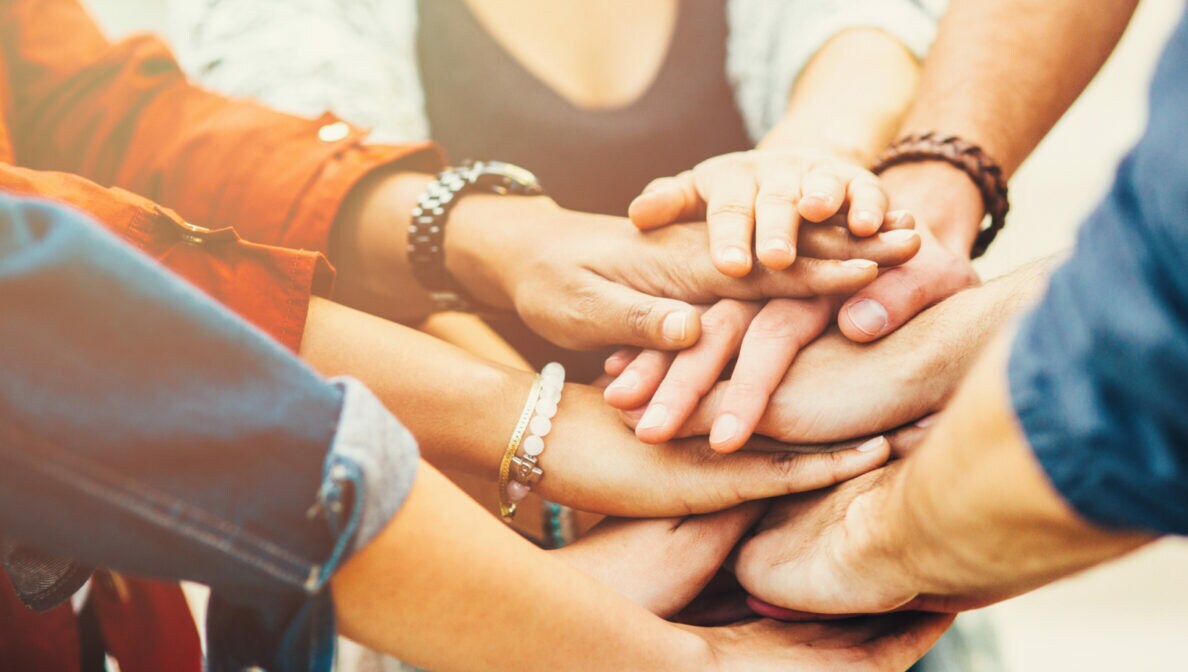 Fünf im Kreis stehende Personen, die ihre Hände in der Mitte übereinanderlegen