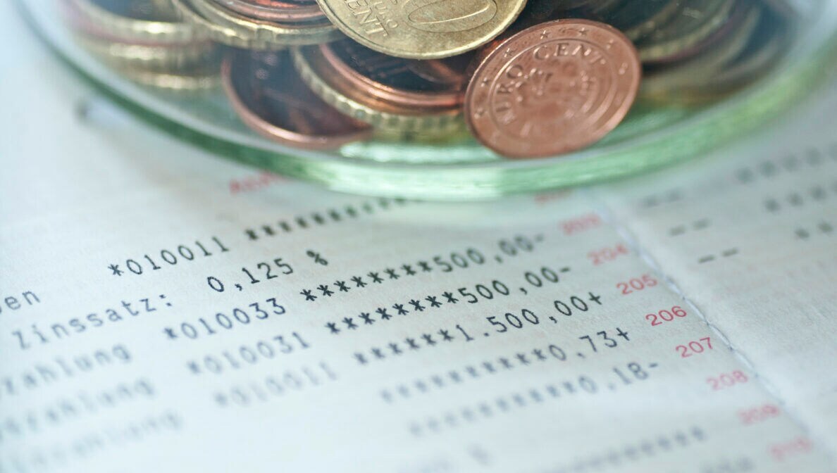Auf einem Kontoauszug liegt ein Stapel Münzen
