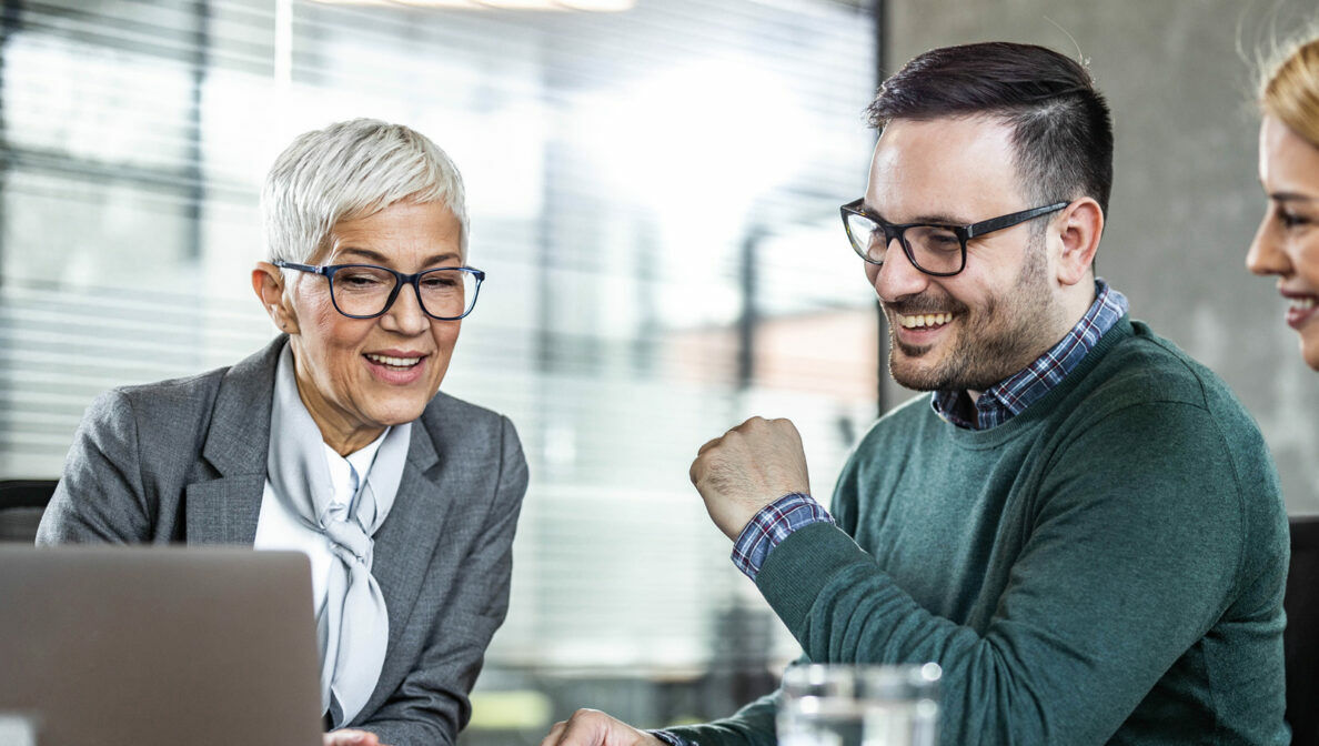 Drei Personen sitzen am Schreibtisch vor einem offenen Notebook