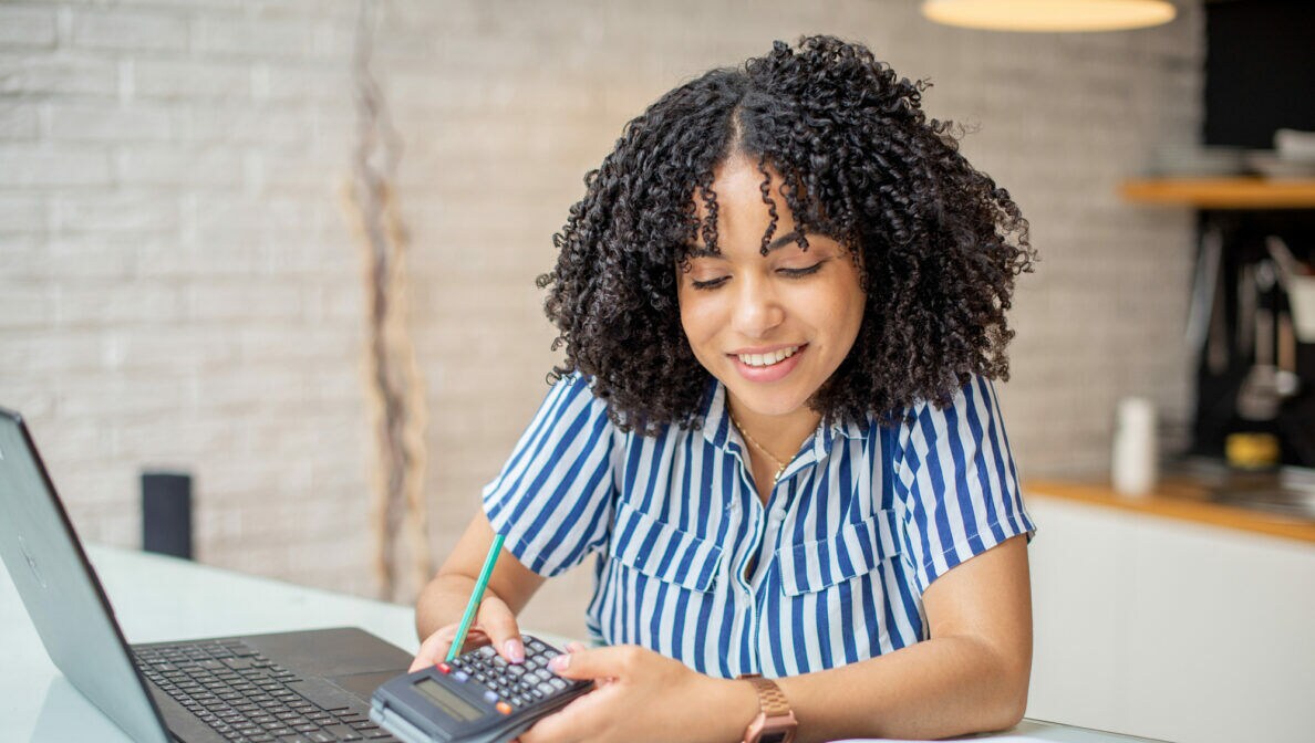 Eine Frau sitzt am Schreibtisch und hält einen Taschenrechner in den Händen