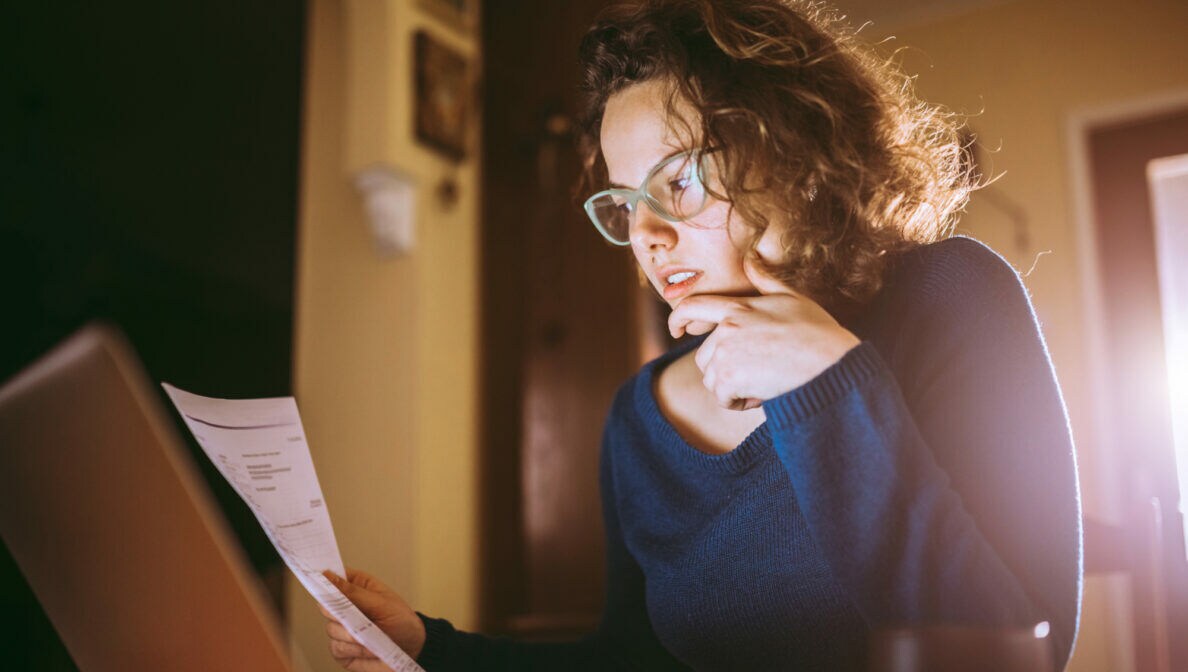 Eine junge Frau sitzt am Tisch und liest Dokumente