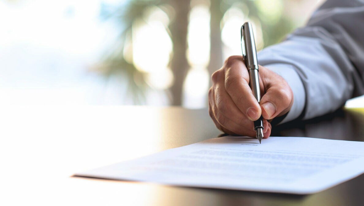 Detailaufnahme einer Hand, die einen Stift hält und ein Dokument unterzeichnet