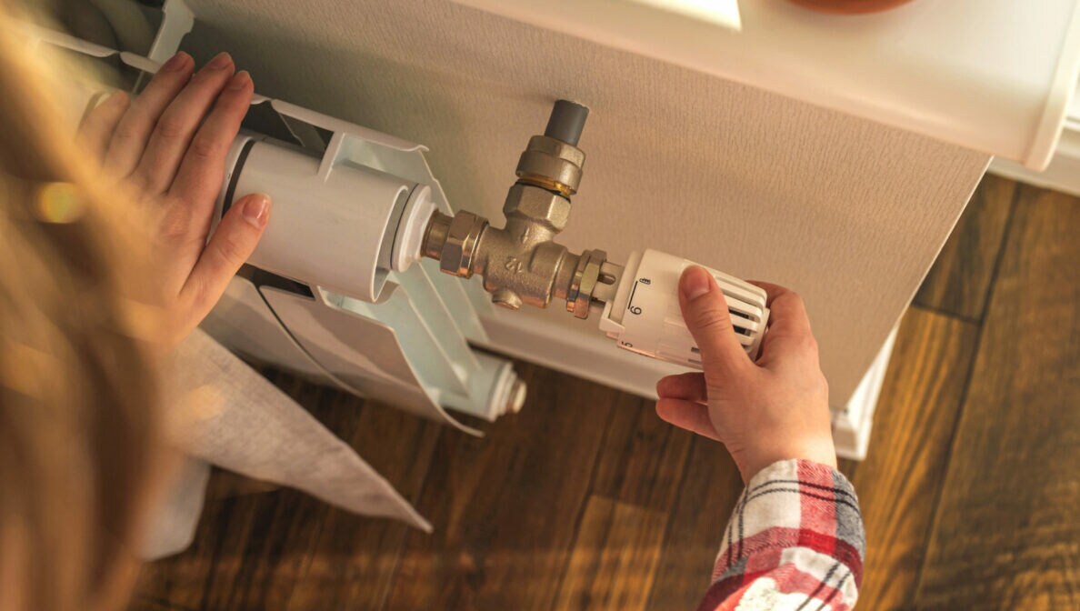 Eine Person dreht am Thermostat eines Heizkörpers