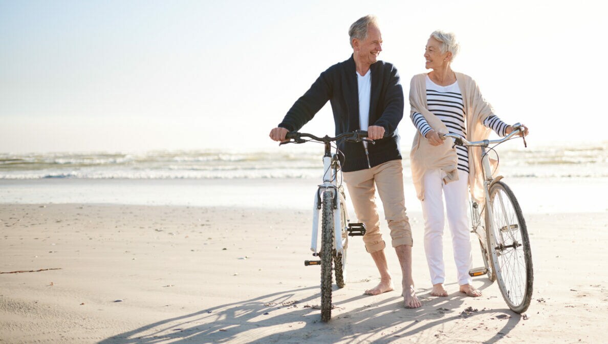 Ein älteres Paar bei Sonnenschein mit Fahrrädern am Strand