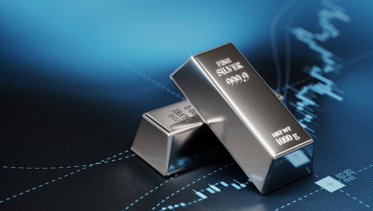 Zwei Silberbarren liegen auf blauem Untergrund, auf dem ein Börsenkurs zu sehen ist