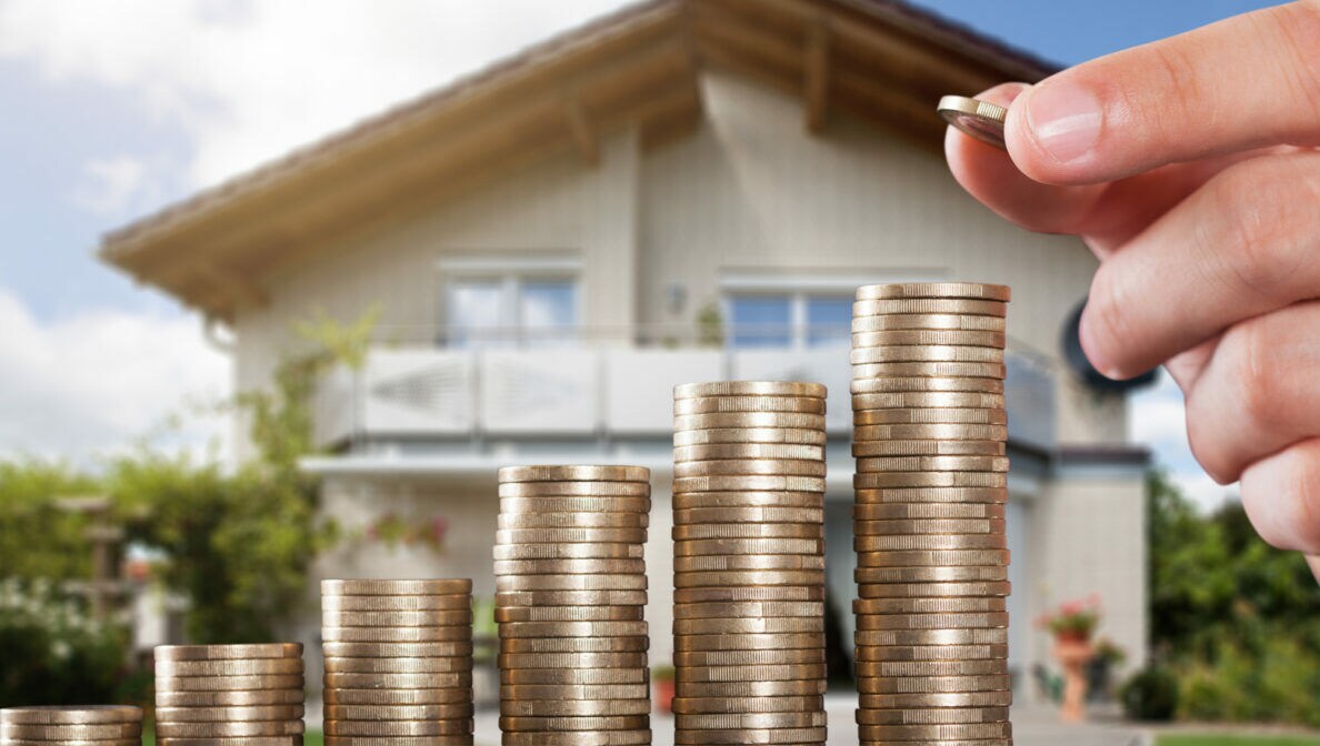 Nach rechts höher werdende Münzstapel. Im Hintergrund ein Einfamilienhaus.