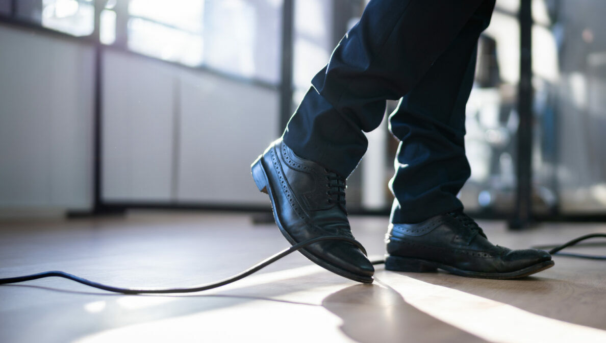 Fokus auf die unteren Beine einer Person, die im Begriff ist, über ein Kabel zu stolpern.