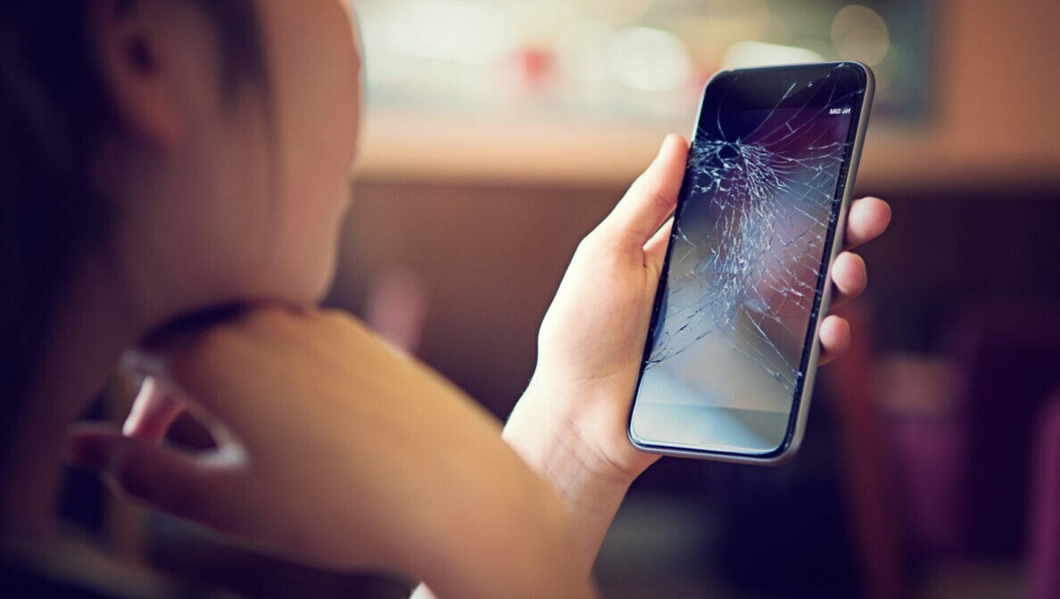 Eine Person betrachtet das Display ihres Smartphones, das zersprungen ist.