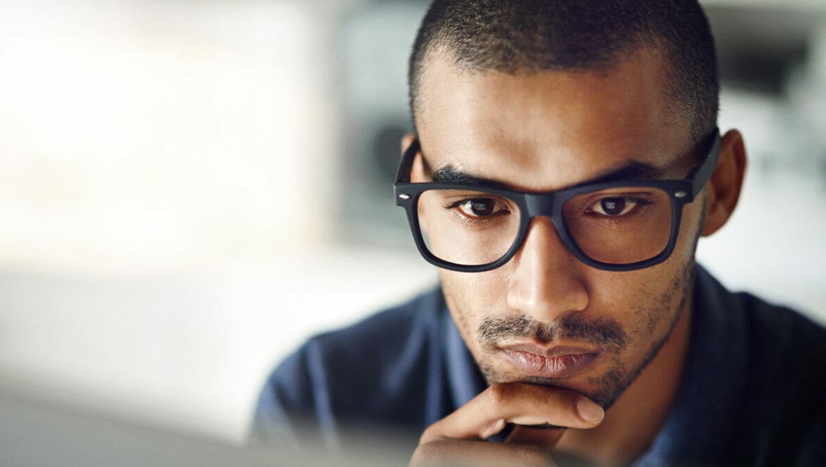 Nahaufnahme des Gesichtes einer Person mit Brille, die konzentriert auf einen Computerbildschirm schaut