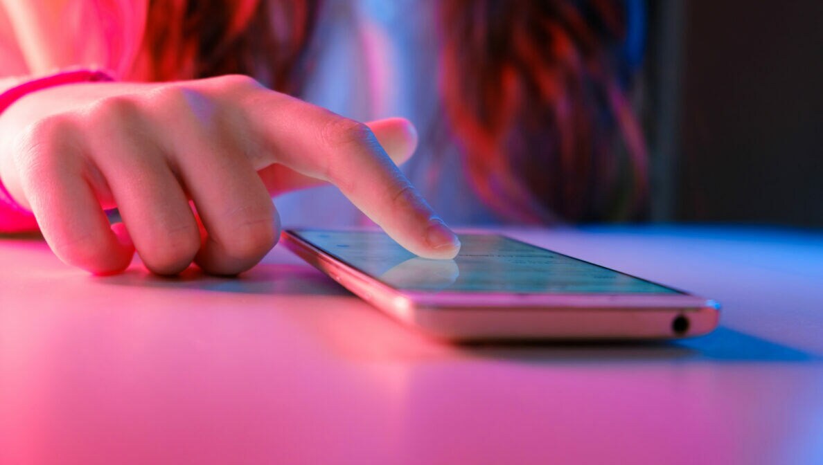 Eine Person tippt mir ihrem Finger auf das Display eines Smartphones, das auf einem Tisch liegt.