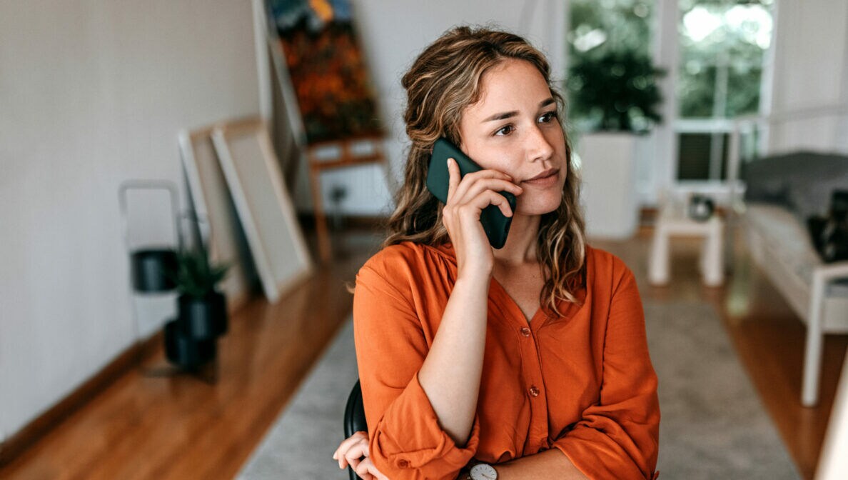 Eine junge Frau beim Telefonieren am Tisch in einer Wohnung