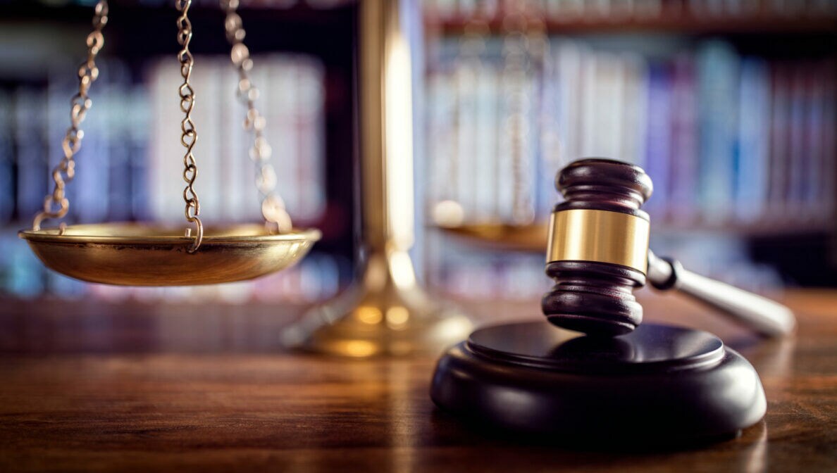 Auf einem Tisch liegt ein Richterhammer auf einem Resonanzblock. Im Hintergrund steht eine Waage.