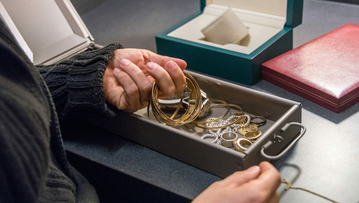 Nahaufnahme einer Person, die goldene Schmuckstücke aus einem Bankschließfach entnimmt