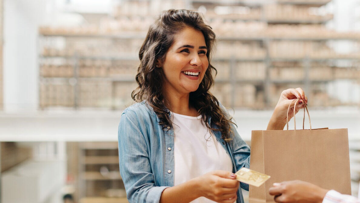 Eine Person bezahlt lachend mit ihrer Bankkarte ihren Einkauf.