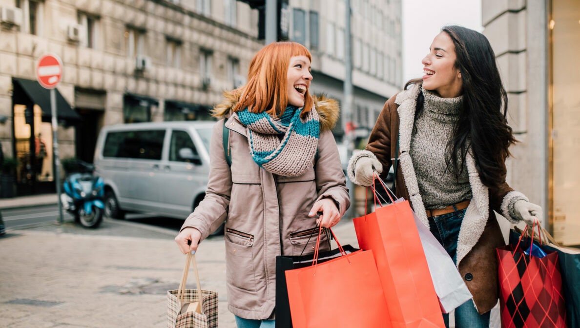 Zwei Personen gehen lachend mit Einkaufstüten über eine Straße.