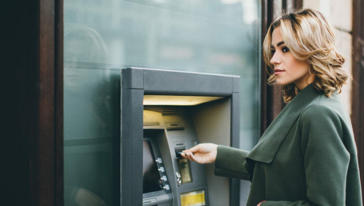 Eine junge Frau schiebt eine Karte in einen Geldautomaten