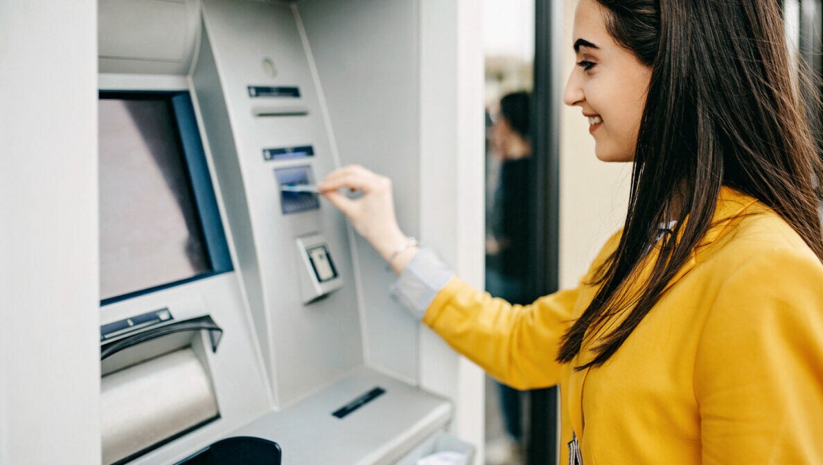 Eine Frau steckt eine Karte in den Eingabeschlitz eines Geldautomaten