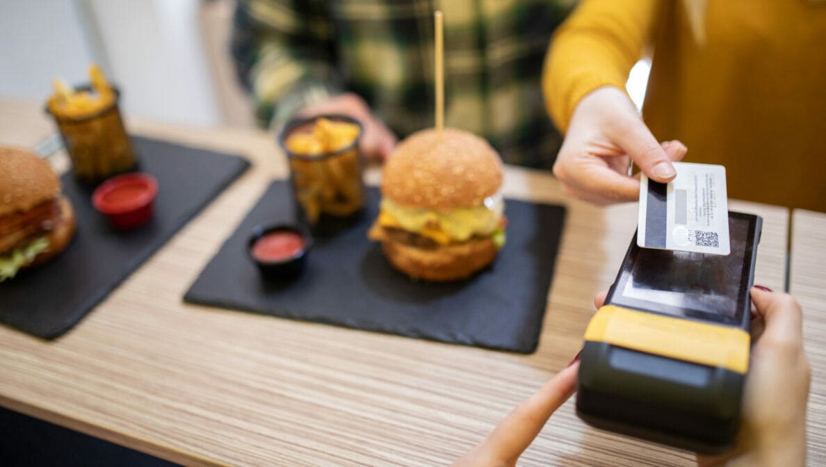 Eine Person bezahlt einen Burger mit einer Kreditkarte.
