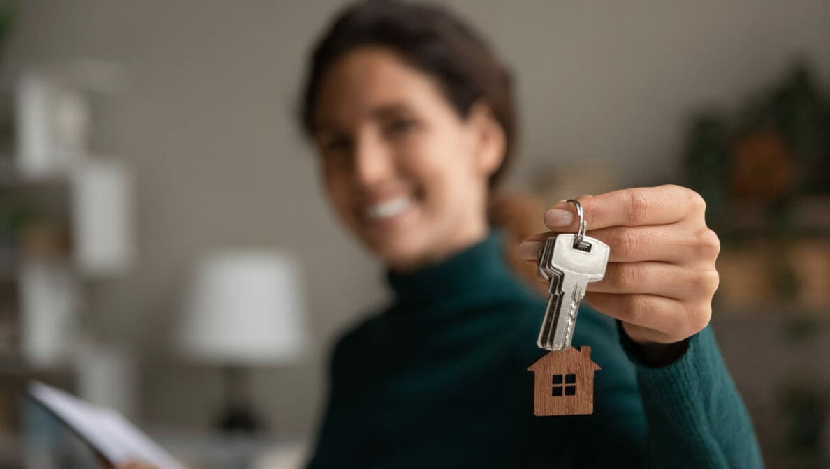 Eine Person hält lächelnd einen Schlüsselbund mit einem Anhänger in Form eines Hauses hoch.