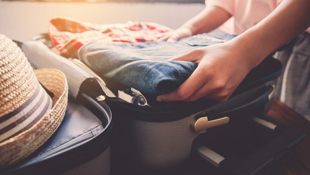 Eine Person legt eine Jeans in einen aufgeklappten Koffer.