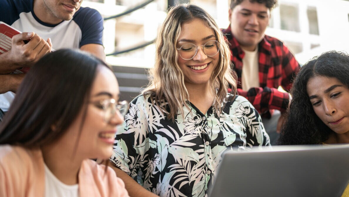 Mehrere junge Personen sitzen in einem Hörsaal um ein Laptop herum.
