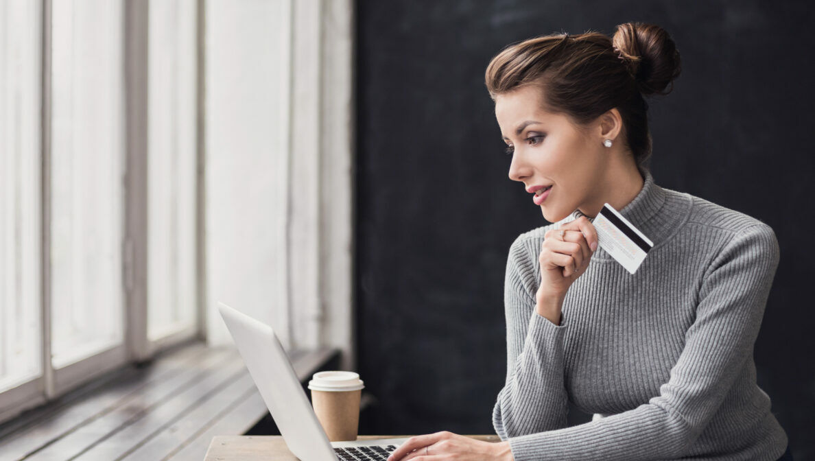 Eine Frau sitzt vor einem Laptop und hält eine Bankkarte in der Hand.