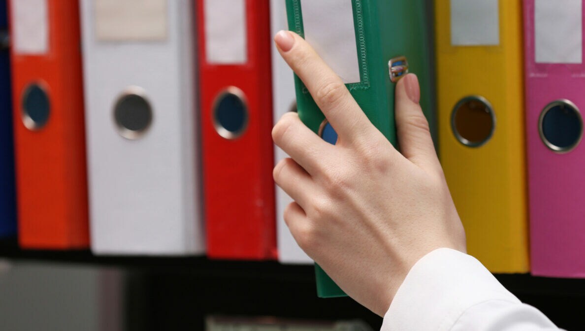 Nahaufnahme einer Hand, die aus einem Regal einen Ordner entnimmt.