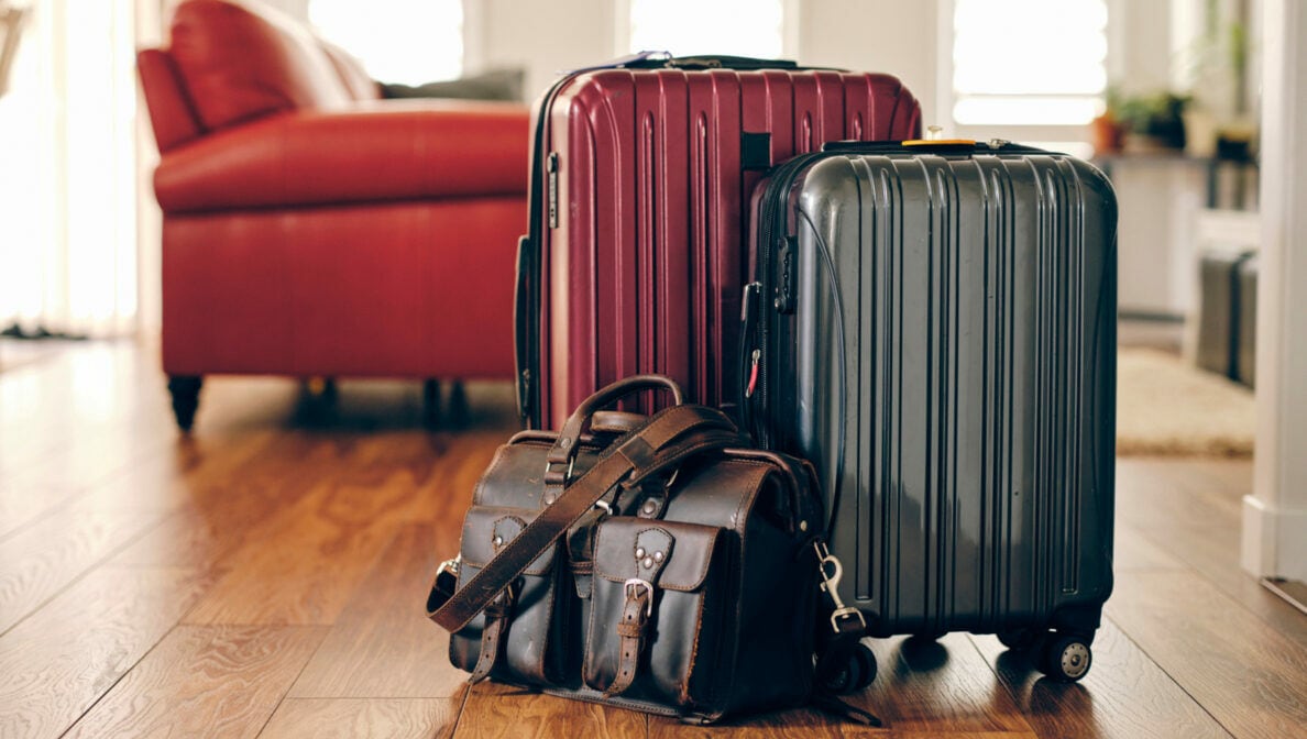 Zwei Koffer und eine Reisetasche stehen vor einem roten Sofa