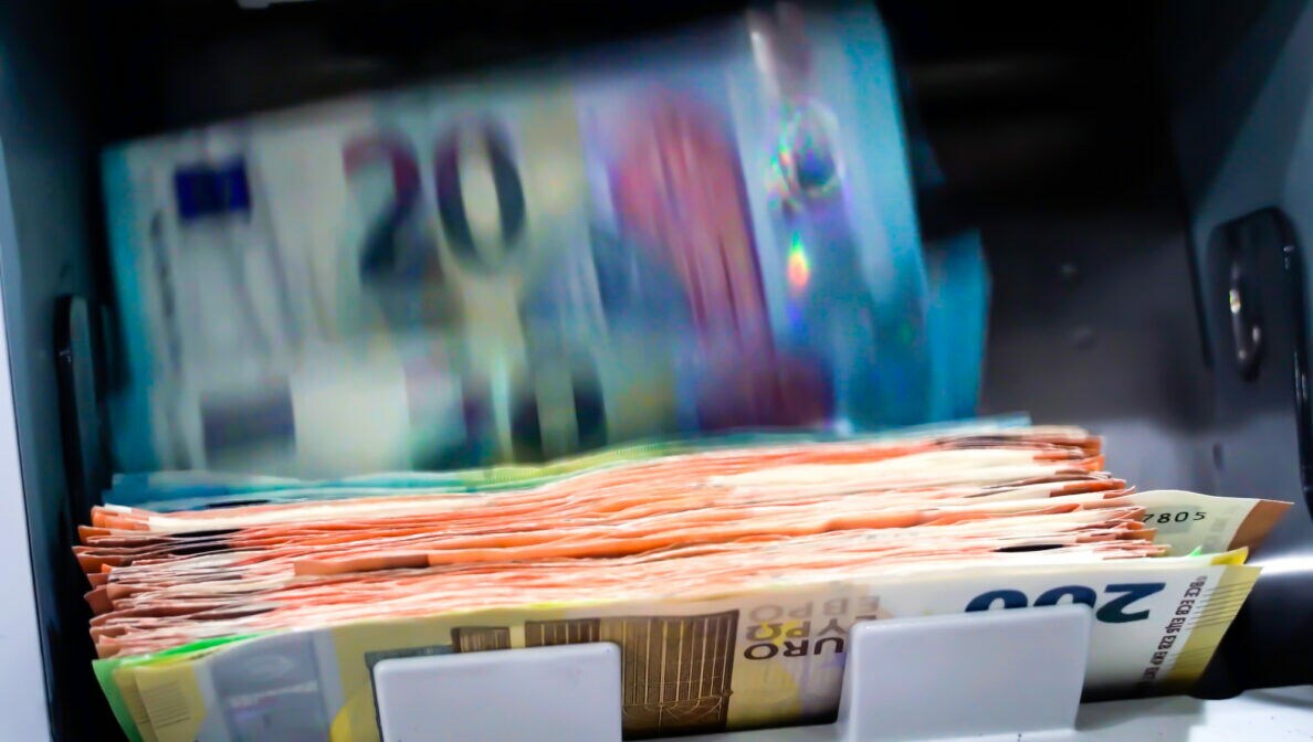 Ein Bündel Geldscheine wird von einem Geldautomaten ausgegeben. Unten liegt ein Stapel 200-Euro-Scheine, der Automat gibt noch 20-Euro-Scheine aus