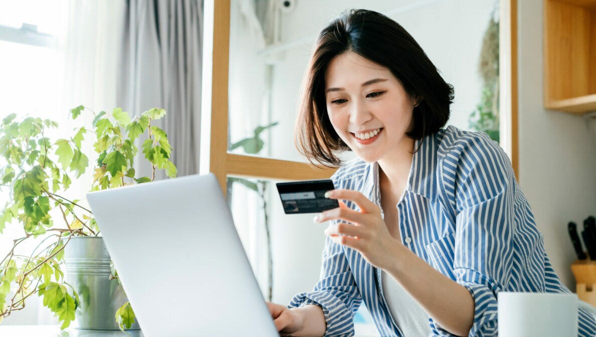 Eine Frau sitzt vor dem Laptop und schaut auf eine Kreditkarte
