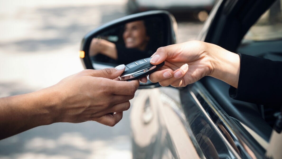 Eine Person sitzt im Auto und bekommt durchs geöffnete Fenster einen Autoschlüssel gereicht.