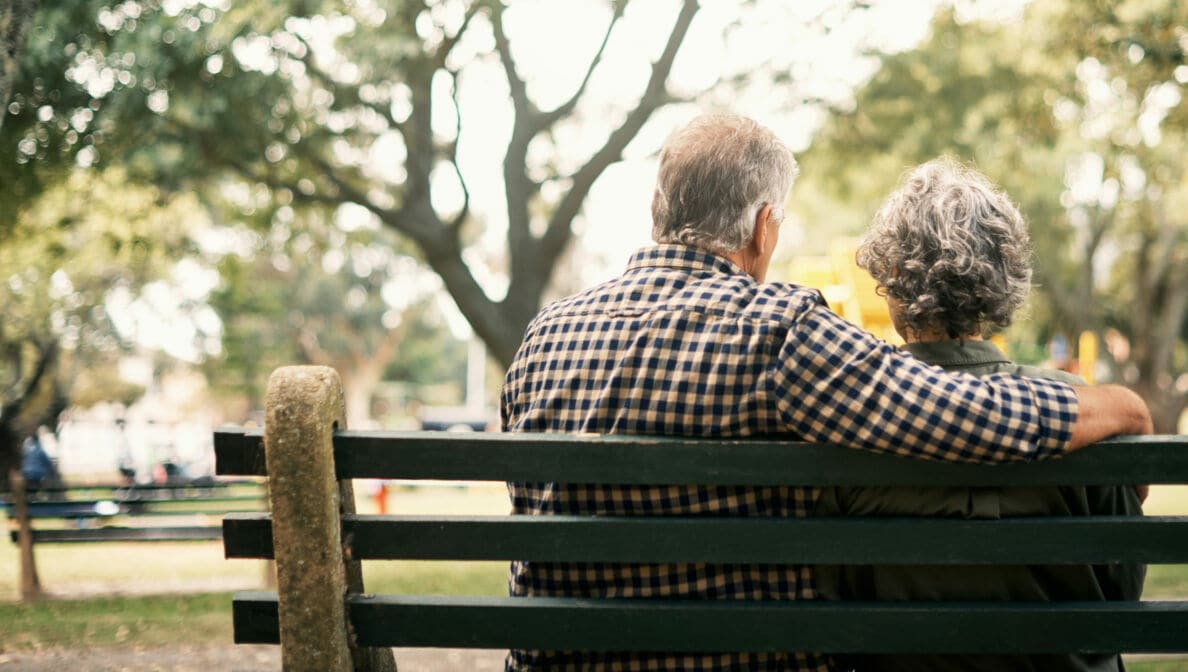 Zwei Personen in der Rückansicht, die in einem Park auf einer Bank sitzen.