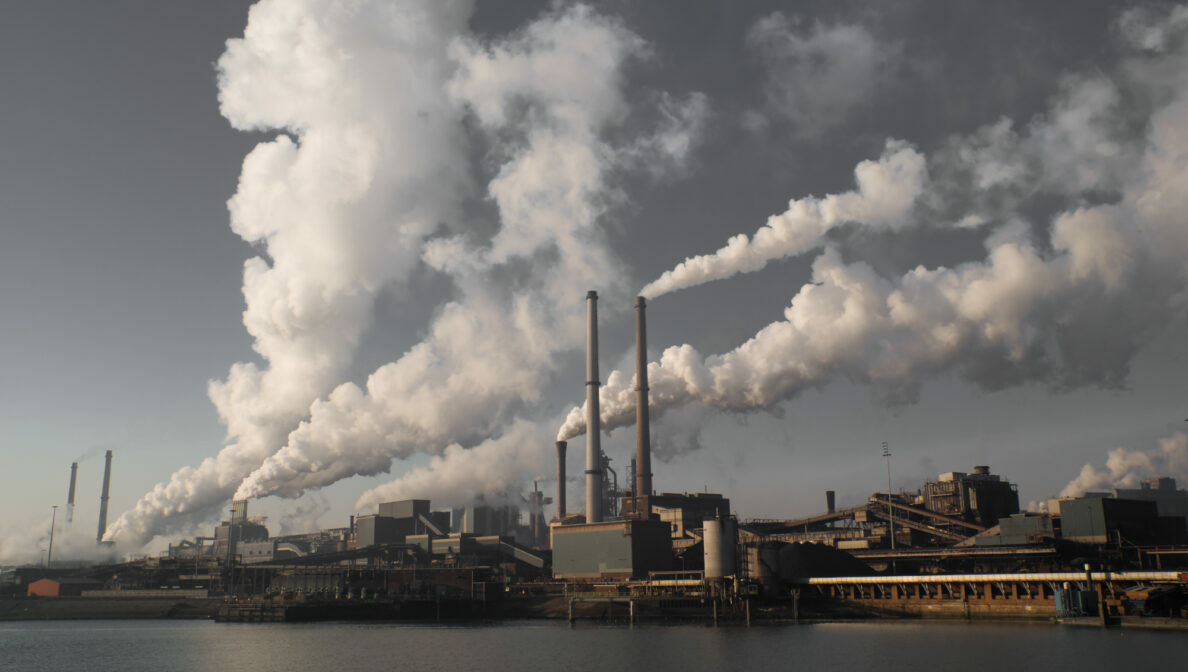 Blick auf einen Industriehafen, an dem mehrere Türme stehen, die qualmen.