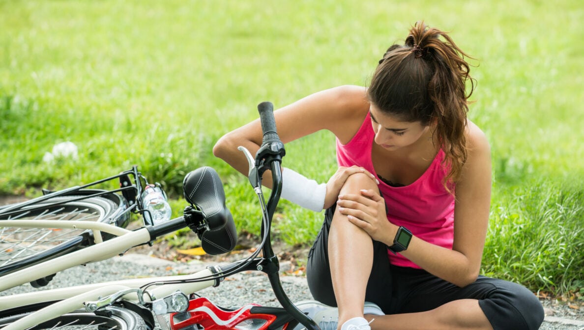Eine Person hält sich ihr Knie, nachdem sie mit dem Fahrrad gestürzt ist.