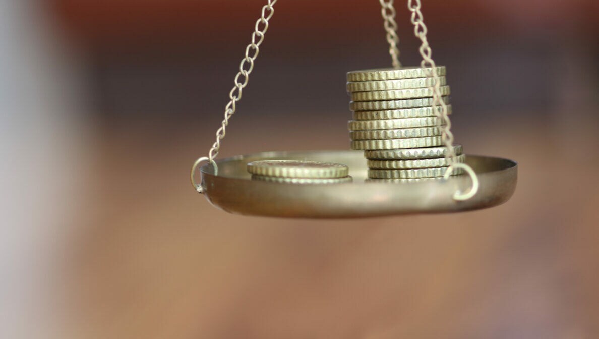 Nahaufnahme einer Waagschale, auf der zwei Münztapel liegen.