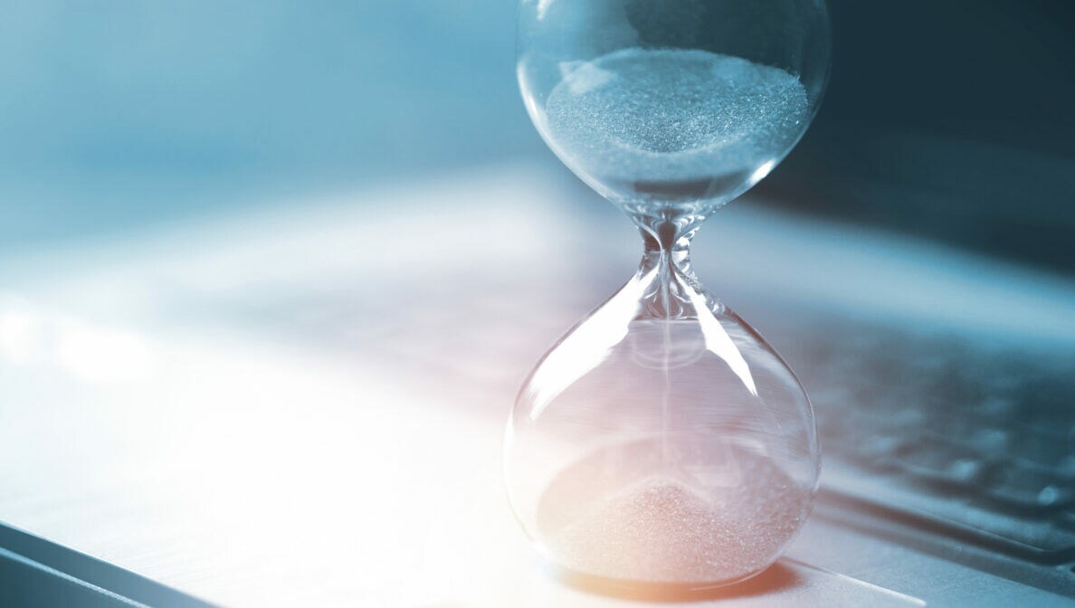 Nahaufnahme einer Sanduhr, die auf dem Touchpad eines Laptops steht.