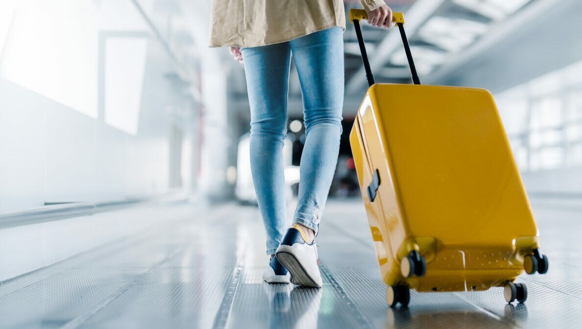 Eine Person in der Rückansicht zieht im Flughafen einen Koffer hinter sich her.